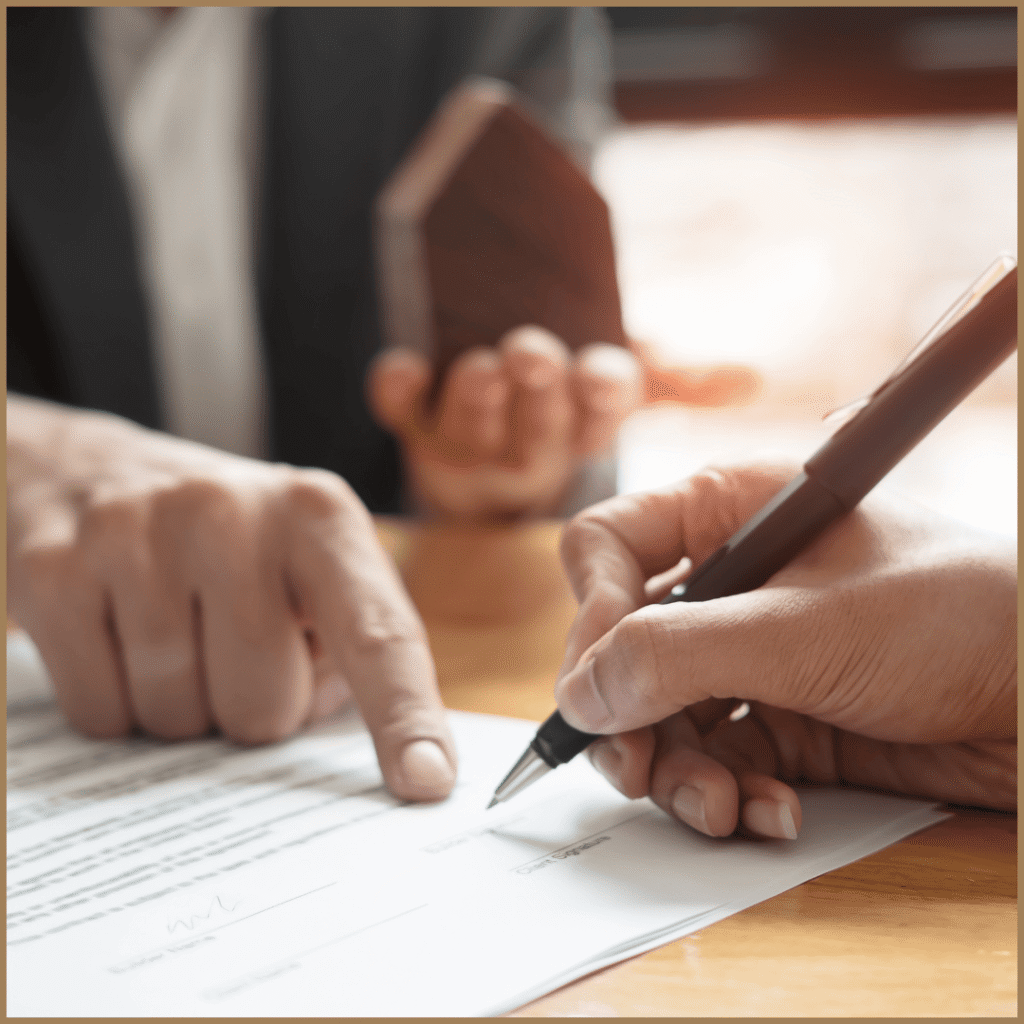 A close-up shot of a person signing a document with a pen, while another person's hand points to a section on the paper.