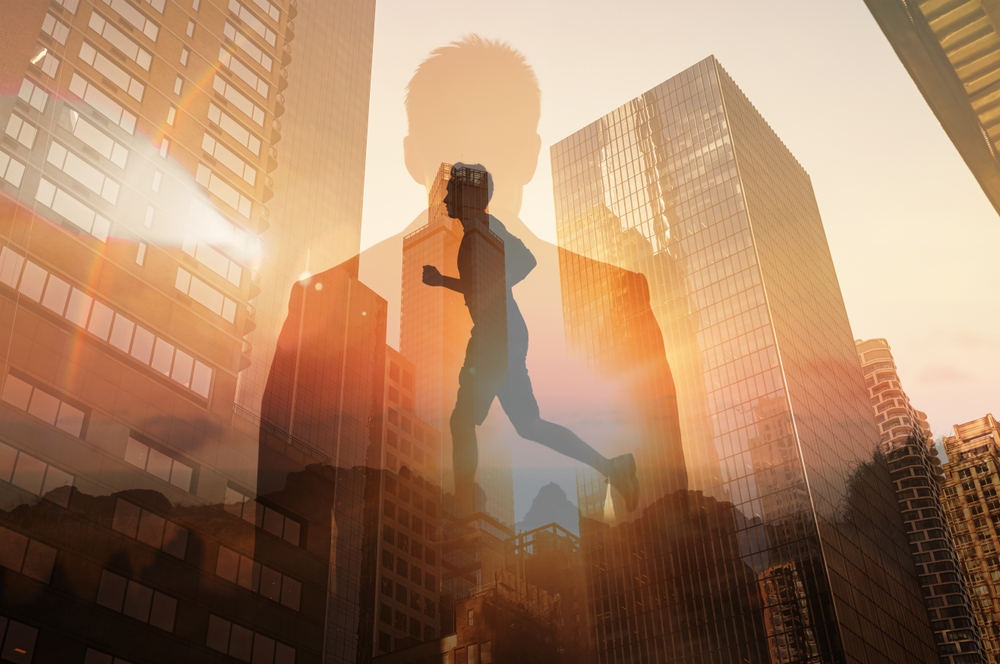 A double exposure image featuring the silhouette of a person running against a backdrop of modern city skyscrapers at sunset or sunrise. The runner's form is overlaid on the buildings, with sun flares and warm orange tones.