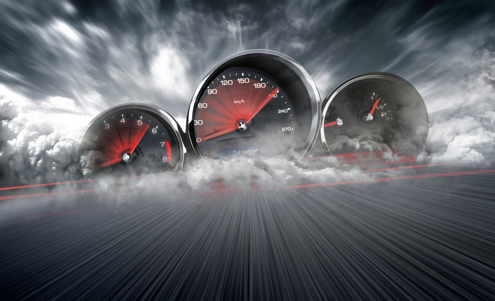 A dramatic image of three vehicle gauges (speedometer, tachometer, fuel gauge) emerging from swirling smoke or clouds, set against a dark, cloudy sky. The speedometer needle points to a high speed, and red motion blur streaks across a road-like surface below.
